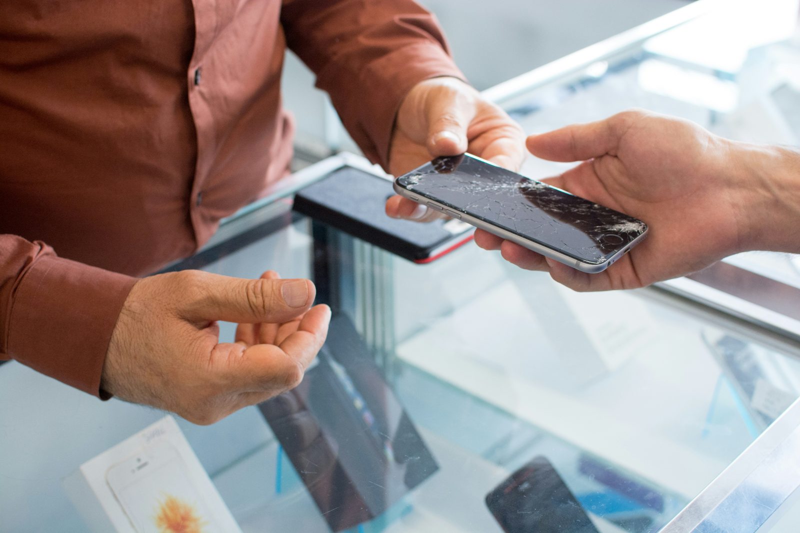 Customer handing a cracked phone to a repair shop staff member at the counter